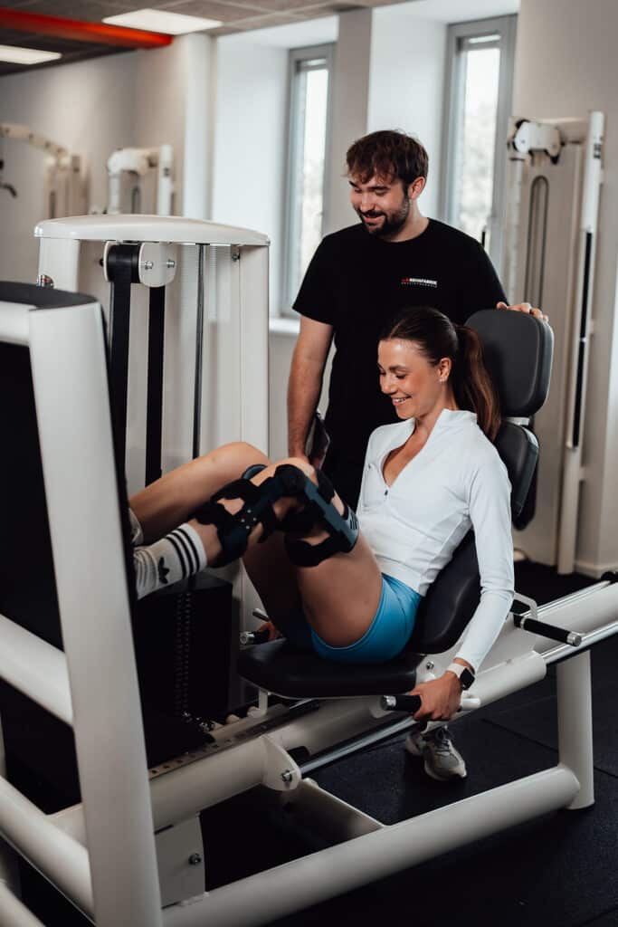 Physical therapy in Bremen at REHAFARBIK. Here, a physical therapist is assisting a patient with the leg press machine.